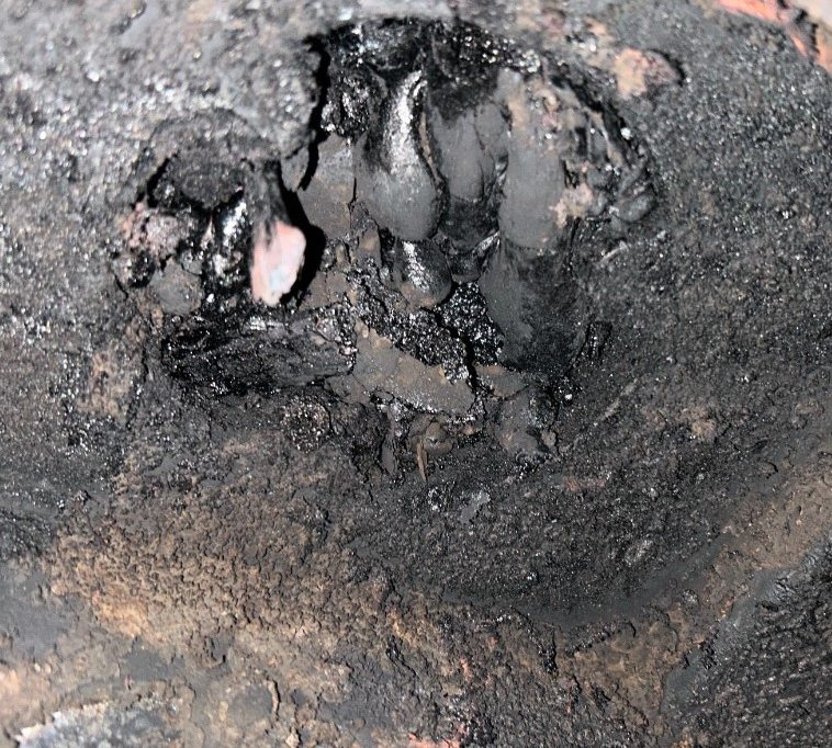 Close-up of blackened, charred surface with uneven texture and various large debris.