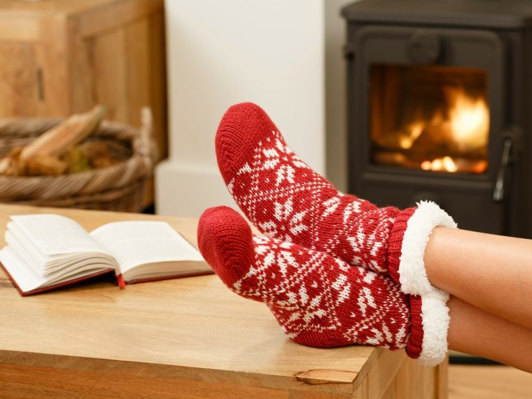 Red patterned socks resting on a wooden table near an open book and a stove.